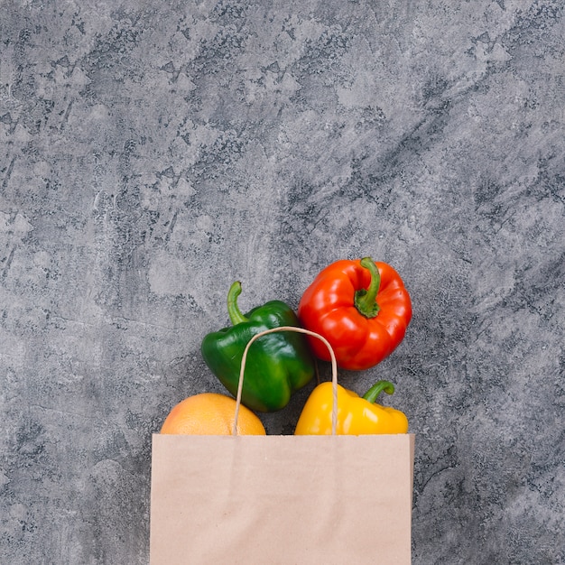 Photo colorful whole capsicum from the paper bag on concrete backdrop