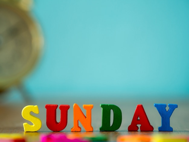 Красочное деревянное слово воскресенье на деревянном столе и винтажном будильнике