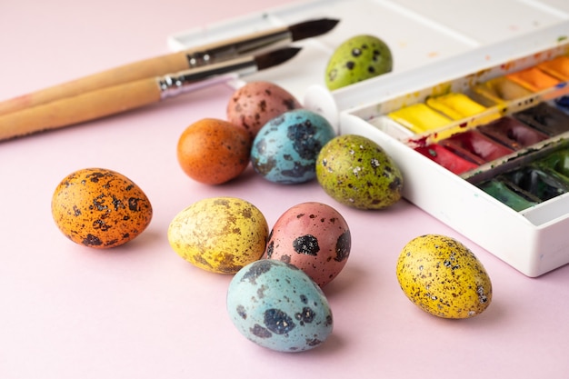 Раскраски яиц на Пасху. Краски, кисти, перепелиные яйца на розовом фоне. Подготовка к празднованию Пасхи, украшения к празднику, фон. Креативная концепция.
