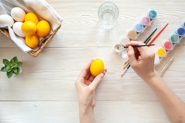 Coloring eggs. The girl draws patterns of silver paint on yellow eggs.