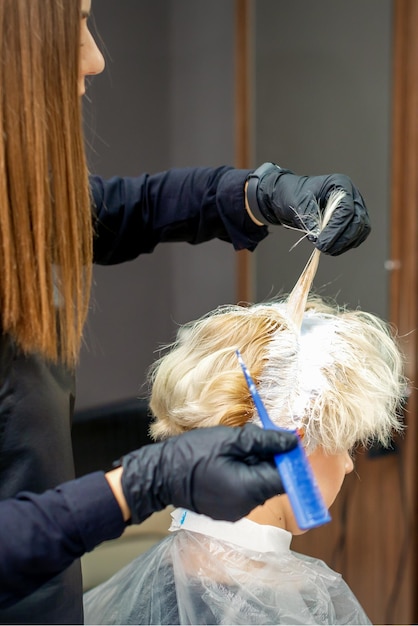 Foto colorare i capelli femminili nel parrucchiere. giovane donna con i capelli tinti dall'estetista presso il salone di bellezza.