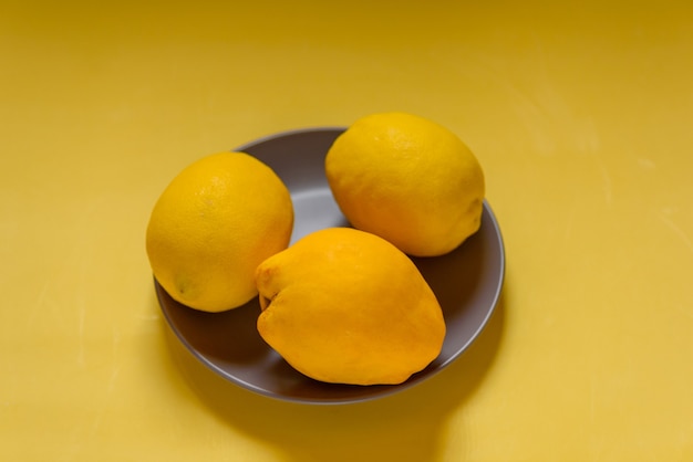 Цвета 2021 года. Лимоны и айва в серой тарелке на желтом фоне. Фрукты