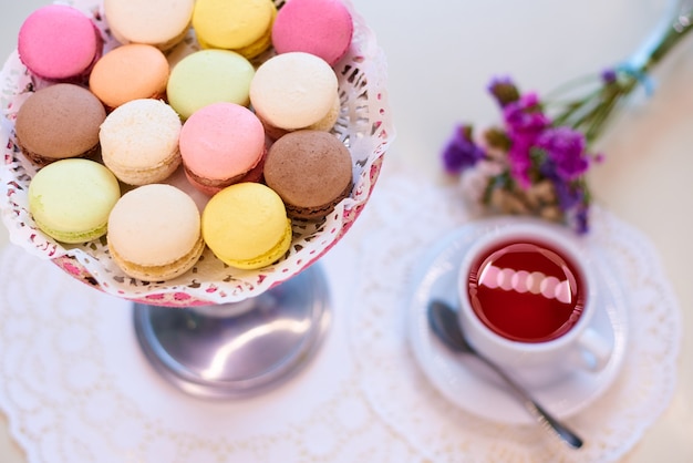 Coloured macaroons with red tea on a table with flowers.