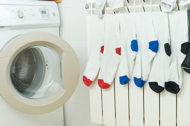 Фото Цветные носки сушатся на радиаторе отопления рядом со стиральной машиной. концепция работы по дому.