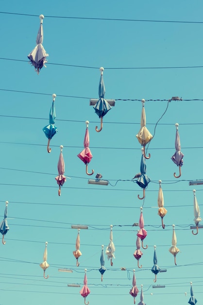 Colourful closed umbrellas with lamps hanging on a wires against the blue sky