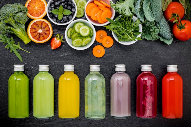 Colourful healthy smoothies and juices in bottles with fresh tropical fruit on dark stone background.