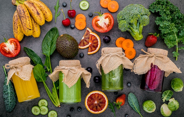 Foto frullati e succhi sani variopinti in bottiglie con frutta tropicale e superfoods freschi su fondo di pietra scuro con lo spazio della copia.