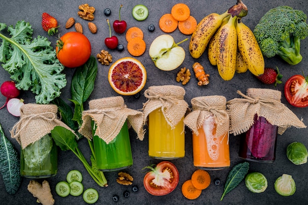 Frullati e succhi sani variopinti in bottiglie con frutta tropicale e superfoods freschi su fondo di pietra scuro con lo spazio della copia.