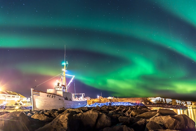 Красочные северные огни с лодкой на переднем плане в исландии
