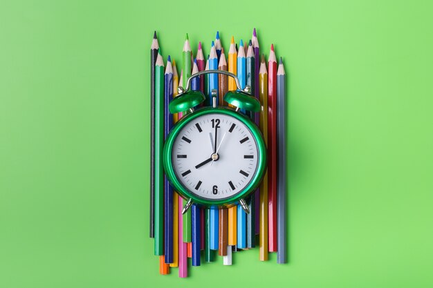 Colourful rainbow pencils and alarm clock on lime green background