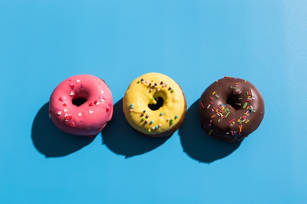 Colourful round donuts at bright blue background. Sweet donuts. Trendy sunlight Summer pattern Minimal summer concept.