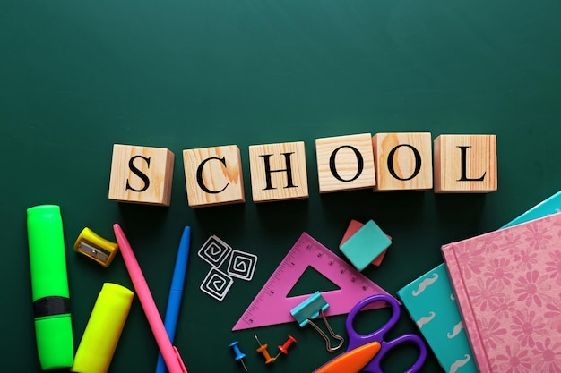 Colourful stationery and word SCHOOL on chalkboard