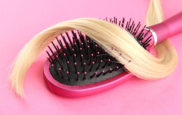 Comb brush with hair on pink background