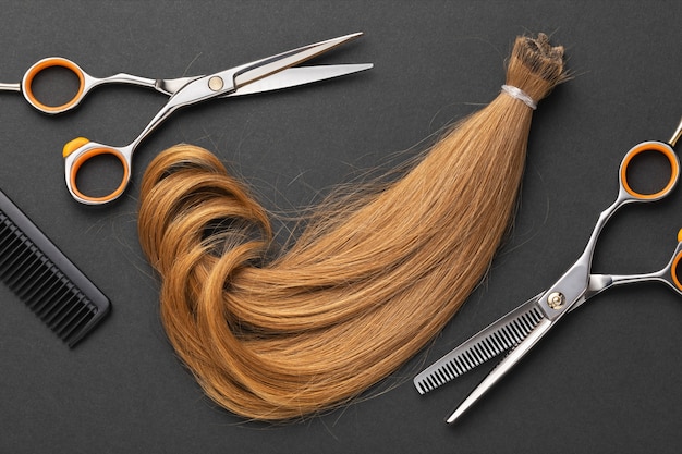 Comb scissors and a cut off pigtail of light color on a dark surface