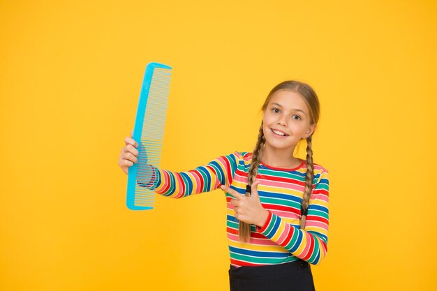 Comb for tangled hair. hairdresser supplies. large comb. girl\
long hair hold enormous comb. hairdresser salon. combing hair.\
cheerful happy smiling little kid with giant comb. professional\
equipment.