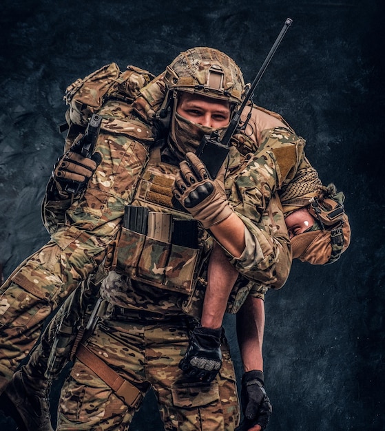 Combat conflict, special mission, retreat. Soldier special forces rescue his wounded teammate carrying him on his shoulders from the battlefield, talking on the radio and calls for support