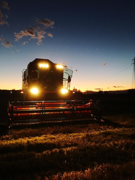 Combine harvester on field against sky during sunset
