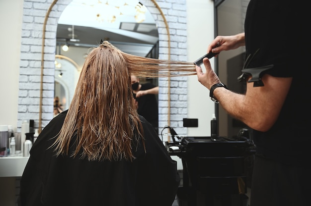 Combing  hair of a beauty salon client trims the ends of the hair to even out the length.