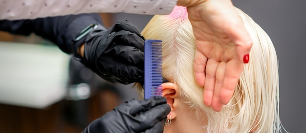 Расчесывание волос расческой во время окрашивания белых волос молодой блондинки в парикмахерской