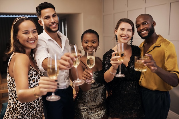 Foto vieni a festeggiare con noi scatto di un gruppo eterogeneo di amici in piedi insieme e con in mano bicchieri di champagne durante una cena di capodanno