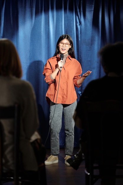 Foto comedian staat tegen blauwe gordijnen.