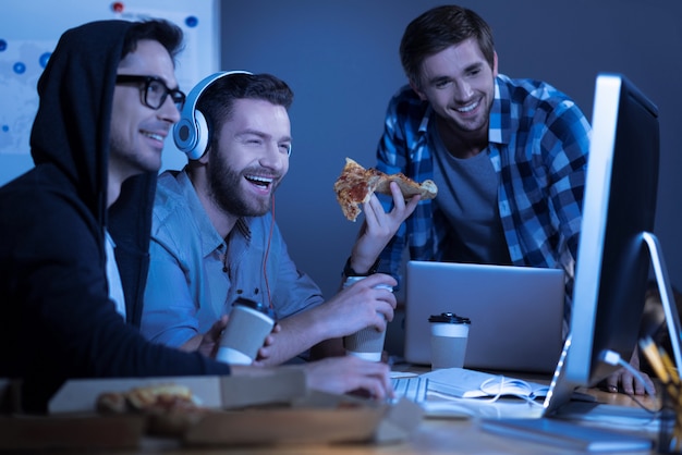 Comedy movie. Happy positive male friend watching a film on the computer and laughing while eating pizza