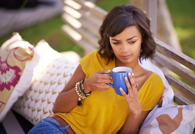 Comfort in een kopje Shot van een jonge vrouw die ontspant met een drankje in de achtertuin