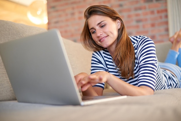 Comfortabel verbonden Shot van een jonge vrouw die thuis een laptop op haar bank gebruikt