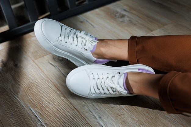 Comfortabele vrouwelijke benen in witte sneakers met platte zolen Close-up van vrouwelijke beenen in lederen sneakers Vrouwelijke zomer sneakers Collectie van vrouwelijke lederen schoenen