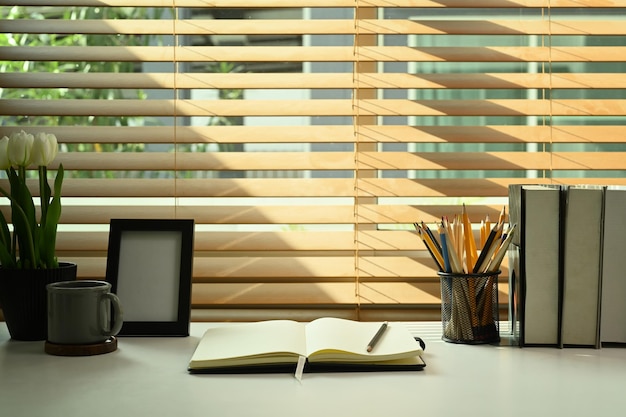 Comfortabele werkplek met boeken fotolijstje koffiekopje potlood houder en bloempot op witte tafel Thuiskantoor bureau