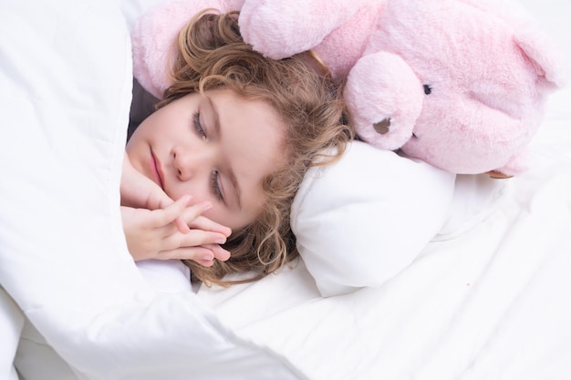 편안한 침대 부드러운 베개 정형외과용 매트리스 아이가 집에서 침대에서 장난감 테디 베어와 함께 자고 있습니다.