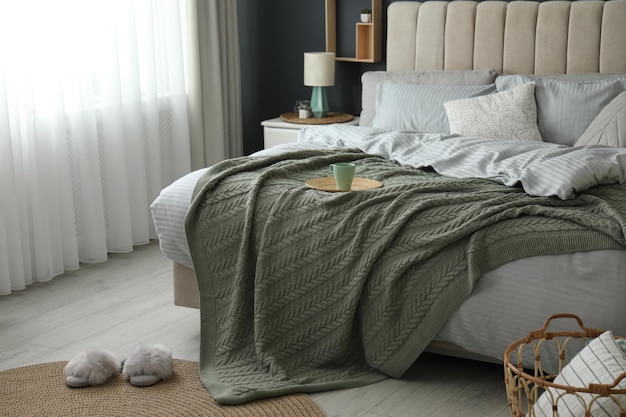 Photo comfortable bed with knitted green plaid in stylish room interior