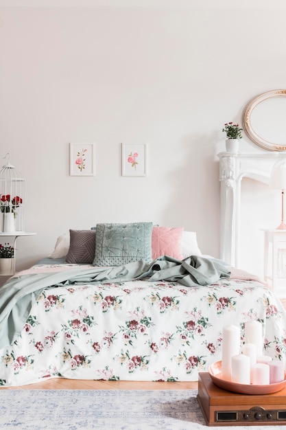 A comfortable bed with a rose pattern coverlet and fluffy pillows in a feminine bedroom interior Real photo