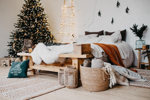 Comfortable bedroom in bohemian interior style with textile sheet on bed christmas tree on background