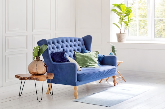 Comfortable classic blue couch with pillows and wooden coffee table in simple white apartment