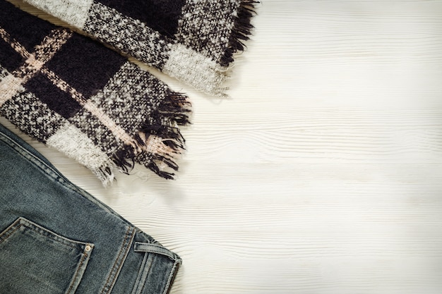 Comfortable clothes. Warm cozy scarf, blue denim jeans on white wooden.