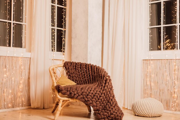 Comfortable modern armchair with brown knitted blanket in interior near window