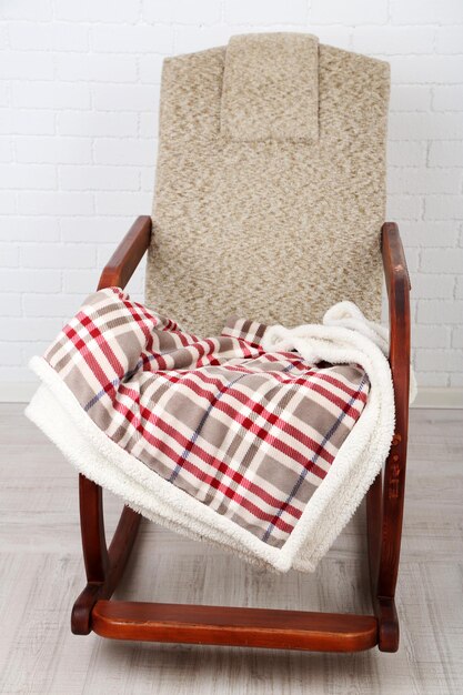 Foto comoda sedia a dondolo con tappeto sul pavimento in legno vicino allo sfondo del muro di mattoni