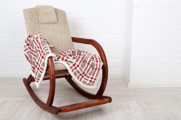 Foto comoda sedia a dondolo con tappeto sul pavimento in legno vicino allo sfondo del muro di mattoni