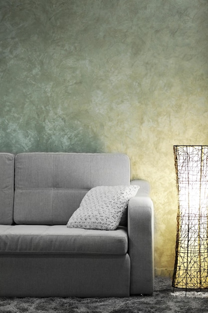 Comfortable sofa and modern lamp on grey wall background