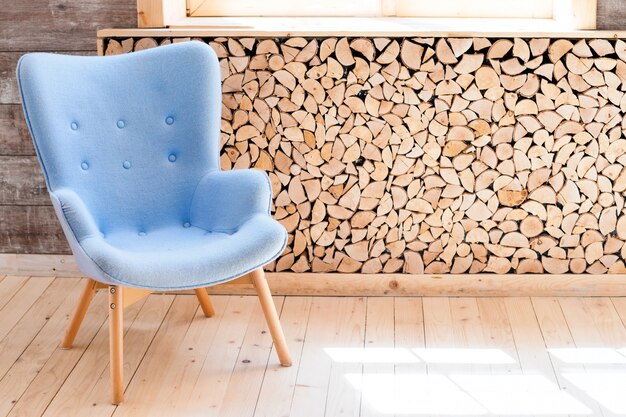 Comfortable soft armchair in scandinavian eco loft apartment. Modern minimalist living room with woodpile.