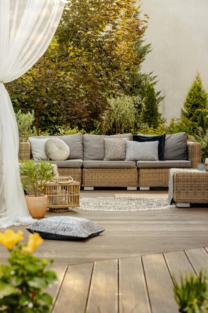 Comfortable wicker garden furniture with grey pillows in beautiful backyard