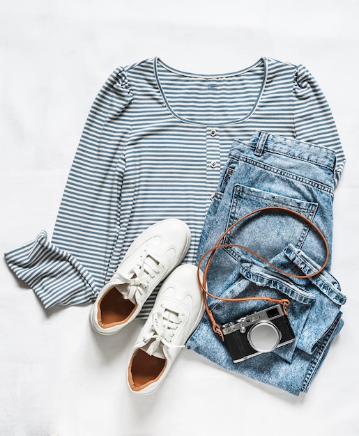 Comfortable women's clothing for walking a knitted Tshirt with long sleeves jeans sneakers and a camera on a light background