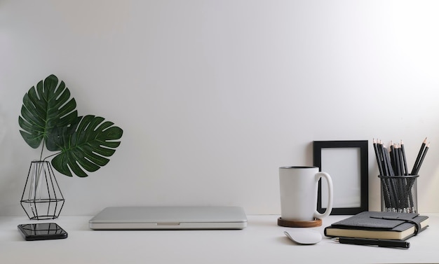 Comfortable workplace with laptop stationery picture frame and potted plant on white tablex9