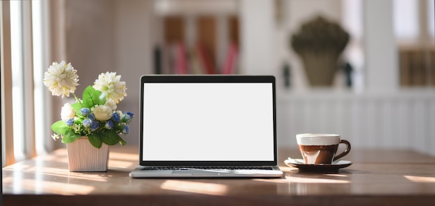 Comfortable workplace with mock up laptop computer, coffee cup and tree pot on wooden table