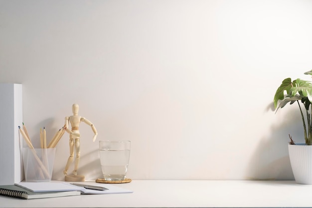 Comfortable workplace with potted plant glass of water and notebook on white table Copy space for your advertise text