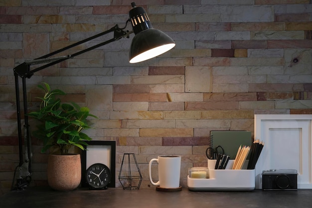 Comfortable workplace with stationery coffee cup lamp and picture frame on black table with brick wall