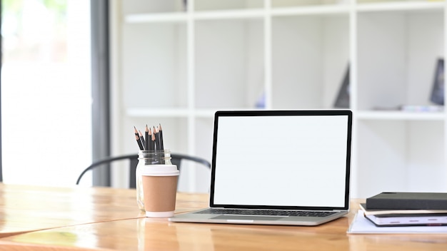 A comfortable workspace is surrounding by a white blank screen computer laptop and office equipment