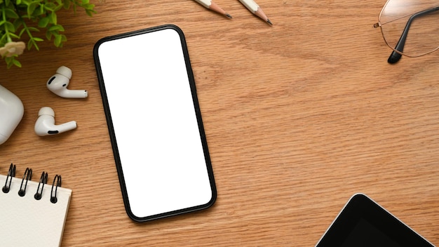 Фото Удобное рабочее пространство с макетом пустого экрана смартфона на фоне деревянного стола, вид сверху