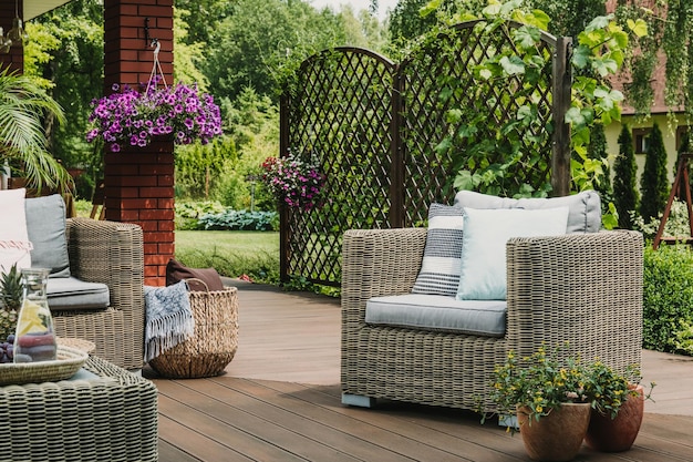 Comfy wicker armchair with pillows on wooden terrace of trendy suburban home